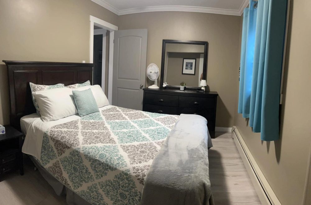 Unit A main bedroom in soothing greys and beachy blues with a made bed and soft light.